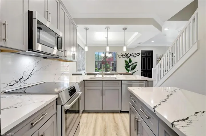 Kitchen with appliances with stainless steel finishes, tasteful backsplash, gray cabinetry, light wood-type flooring, and ornamental molding