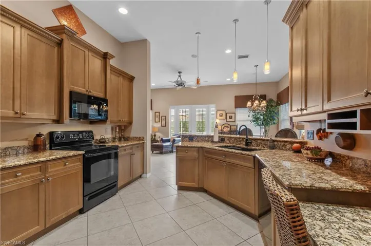 Kitchen with ceiling fan with notable chandelier, decorative light fixtures, black appliances, light stone counters, and sink