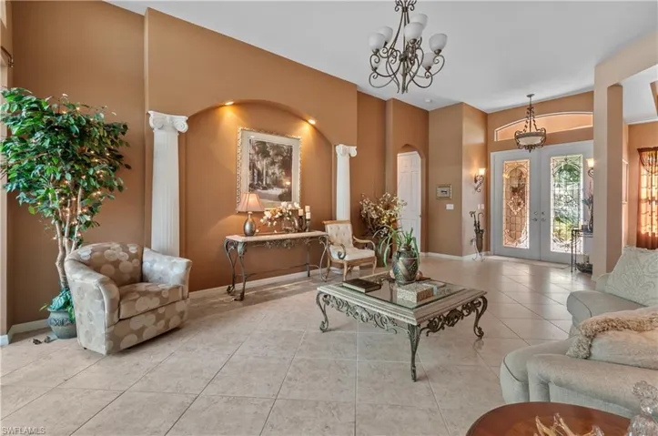 Tiled living room with french doors, ornate columns, and an inviting chandelier