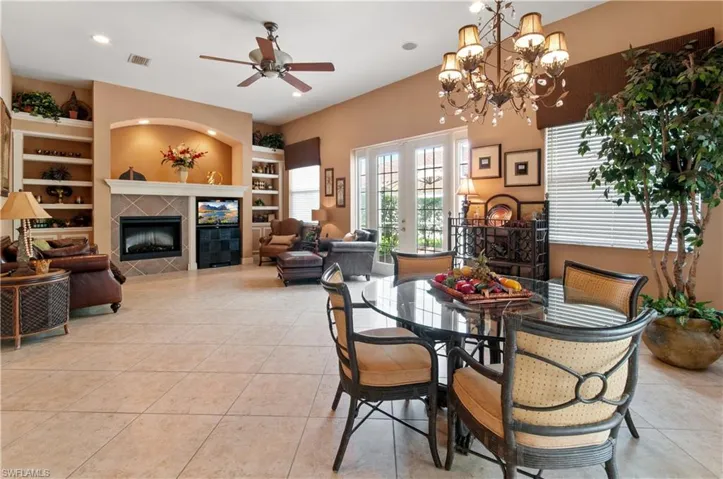 Dining room featuring built in shelves, a tiled fireplace, ceiling fan with notable chandelier, and light tile patterned floors