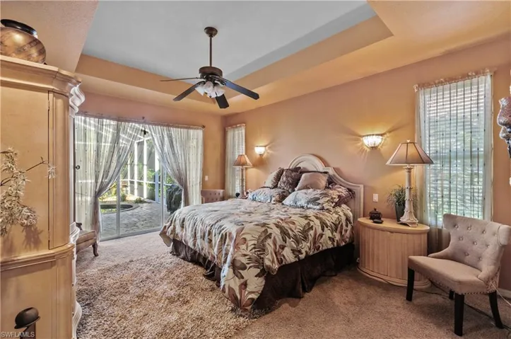 Carpeted bedroom with ceiling fan, a raised ceiling, and access to exterior