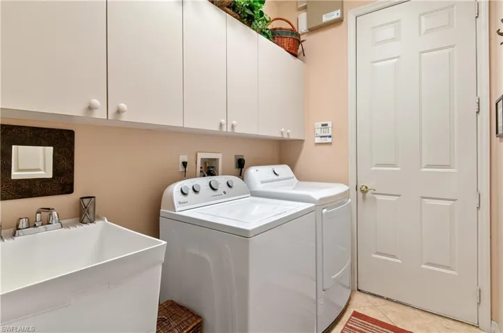 Clothes washing area with washer and dryer, cabinets, sink, and light tile patterned flooring