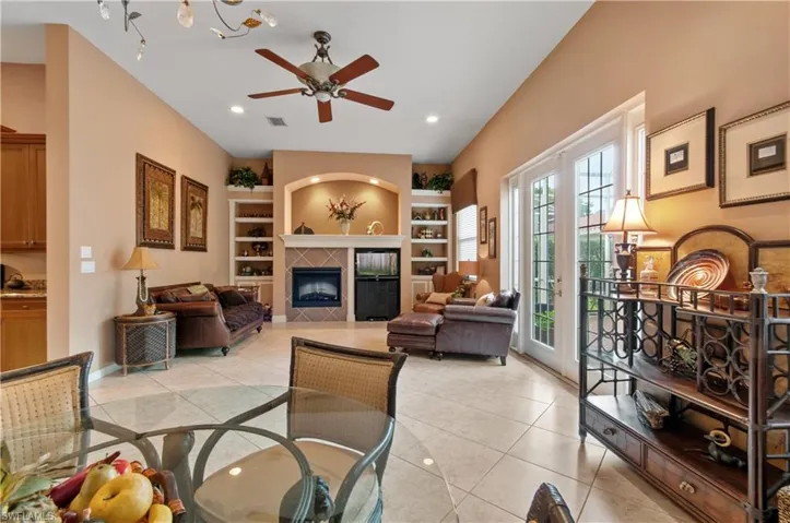 Tiled living room featuring built in shelves, ceiling fan, a fireplace, and french doors