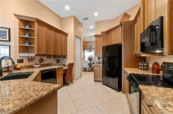 Kitchen featuring black appliances, light stone countertops, a wealth of natural light, and sink