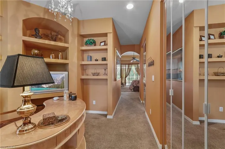 Corridor featuring lofted ceiling, built in shelves, carpet flooring, and an inviting chandelier