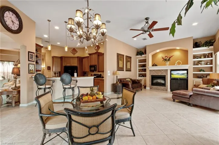 Dining room featuring built in features, light tile patterned floors, ceiling fan with notable chandelier, and a tile fireplace