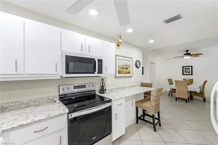 Kitchen with stainless steel electric range oven, ceiling fan, white microwave, white cabinetry, and recessed lighting