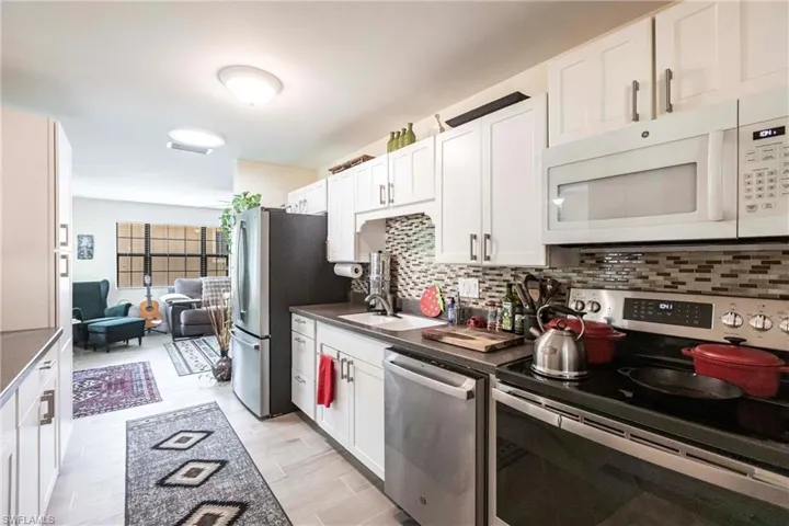 Kitchen featuring stainless steel appliances, white cabinetry, decorative backsplash, and light wood-style flooring