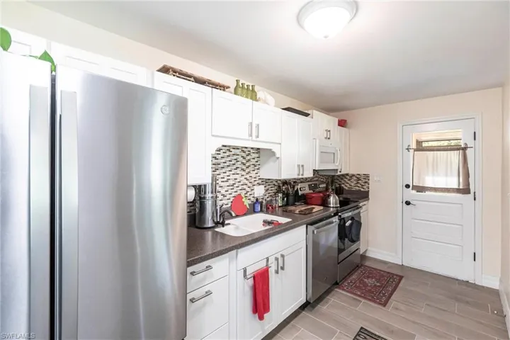 Kitchen with appliances with stainless steel finishes, dark countertops, wood finish floors, white cabinets, and backsplash