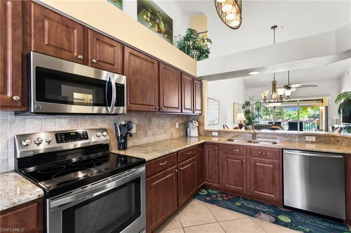Kitchen featuring light tile flooring, pendant lighting, light stone counters, sink, and appliances with stainless steel finishes