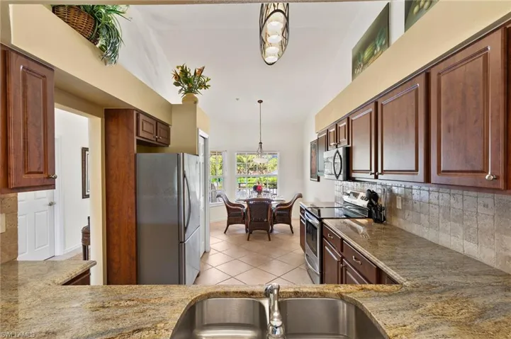 Kitchen featuring decorative light fixtures, stainless steel appliances, backsplash, light stone countertops, and sink