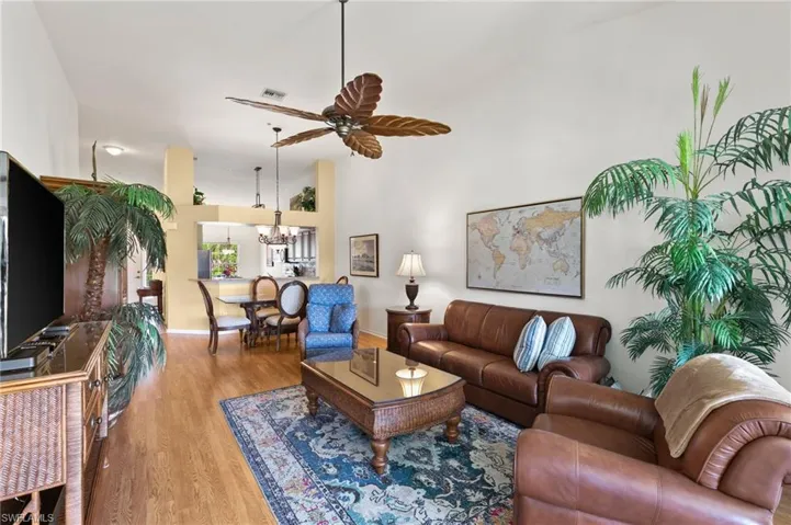 Living room featuring high vaulted ceiling, wood-type flooring, and ceiling fan with notable chandelier