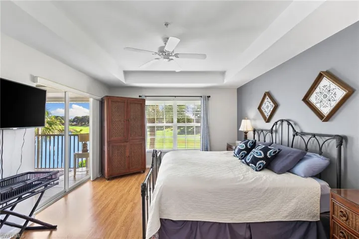 Bedroom featuring a tray ceiling, access to exterior, light hardwood / wood-style floors, and ceiling fan