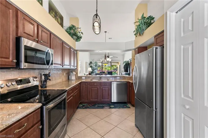 Kitchen with appliances with stainless steel finishes, light stone counters, pendant lighting, tasteful backsplash, and ceiling fan