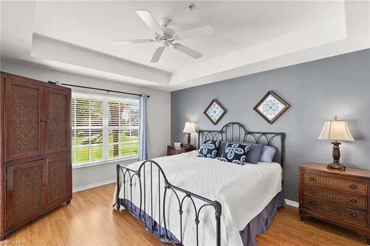 Bedroom with a tray ceiling, ceiling fan, and light wood-type flooring