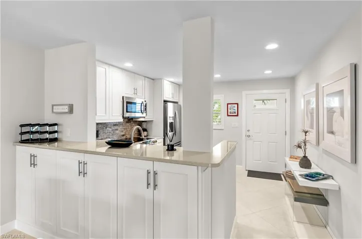 Kitchen with a peninsula, white cabinetry, stainless steel appliances, light stone countertops, and recessed lighting
