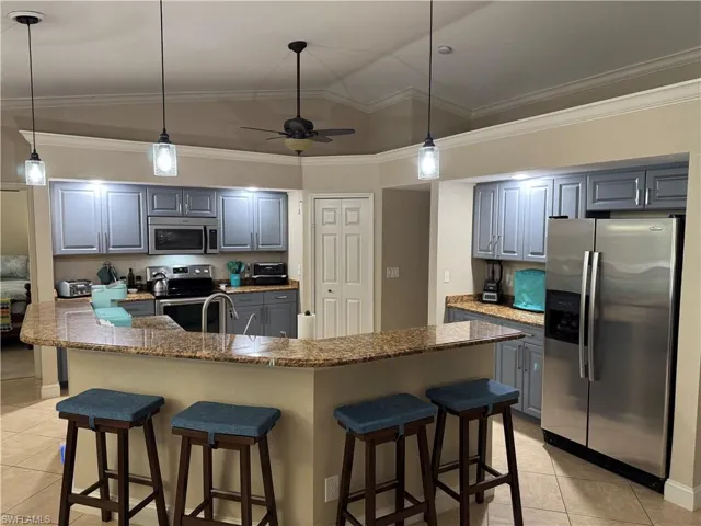 Kitchen with a brick fireplace, stainless steel fridge, light tile patterned floors, ceiling fan, and crown molding