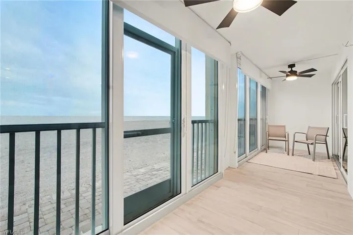 Expansive outdoor balcony featuring large sliding glass doors, light wood-finish flooring, and black ceiling fans