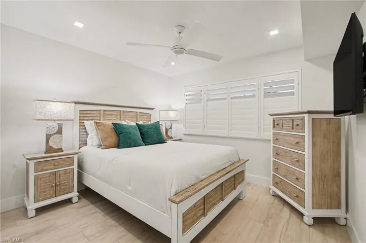 Spacious bedroom featuring light wood-finish flooring, recessed lighting, ceiling fan, and white plantation shutters