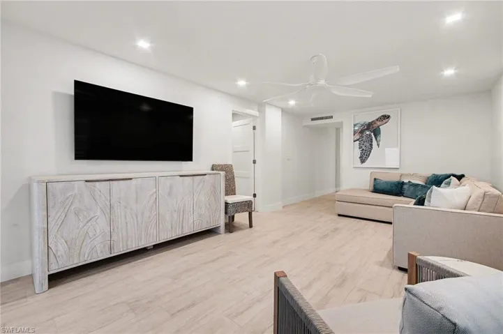 Recessed lighting illuminates an entertainment space featuring wood-finish flooring and a white ceiling fan