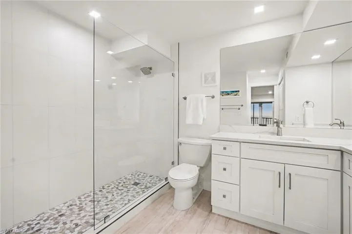 Bathroom featuring a frameless glass shower enclosure with pebble floor, white wall tile, and a rainfall shower head
