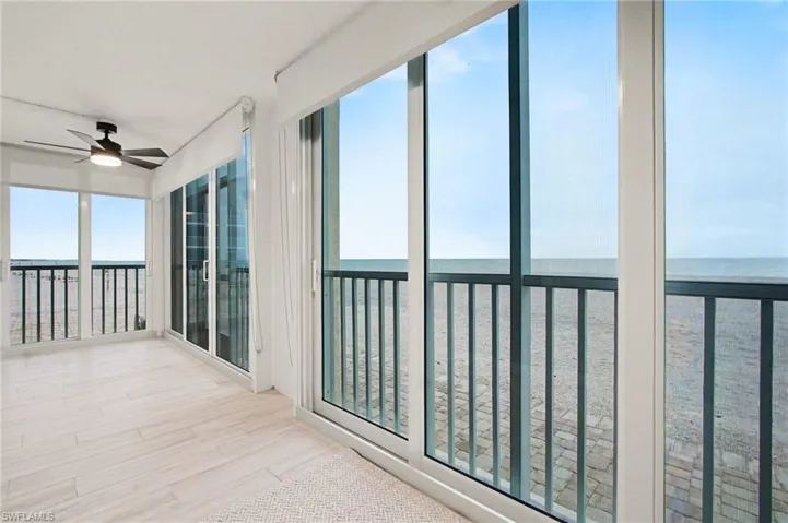Expansive room featuring light wood-finish flooring and panoramic sliding glass doors opening to a balcony with metal railings