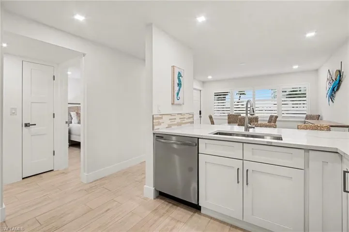 Contemporary kitchen island with a stainless steel undermount sink, gooseneck faucet, white shaker cabinetry, stainless steel dishwasher, and light-toned tile backsplash