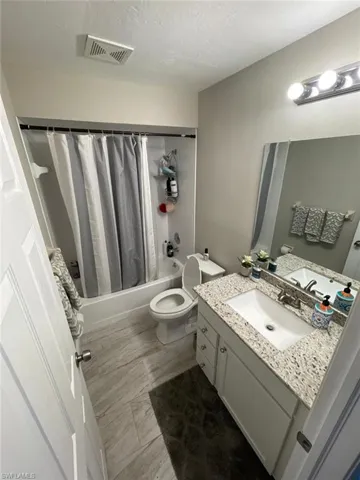 Bathroom featuring shower / tub combo, toilet, vanity, and a textured ceiling