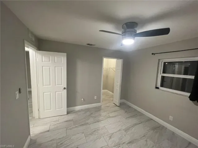 Unfurnished bedroom featuring light marble finish flooring, baseboards, a closet, a walk in closet, and a ceiling fan