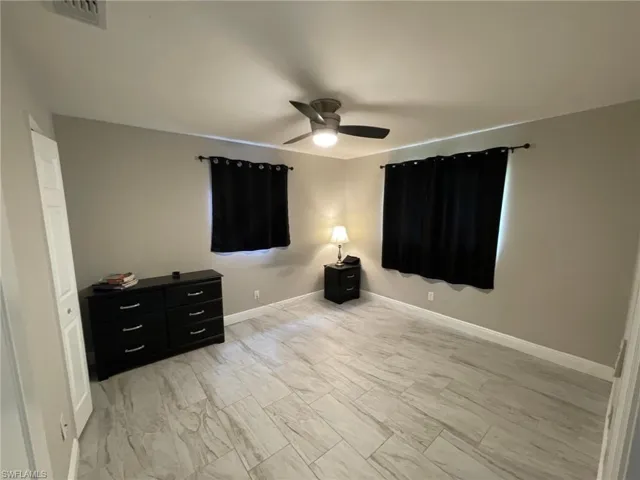 Unfurnished bedroom featuring a ceiling fan, baseboards, and light marble finish flooring