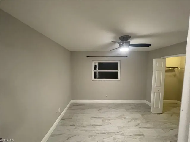 Unfurnished bedroom featuring baseboards, light marble finish flooring, ceiling fan, and a walk in closet