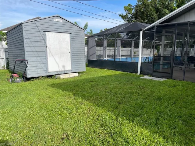 View of green lawn featuring a storage unit, an outbuilding, and glass enclosure