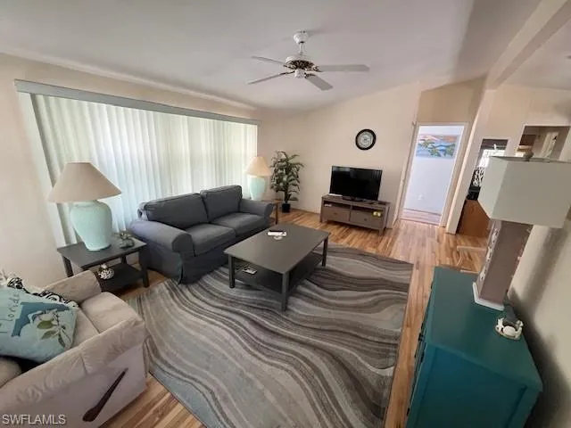 Living room featuring vaulted ceiling, ceiling fan, and light wood-type flooring