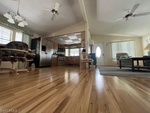 Living room with lofted ceiling, sink, ceiling fan with notable chandelier, and light hardwood / wood-style flooring