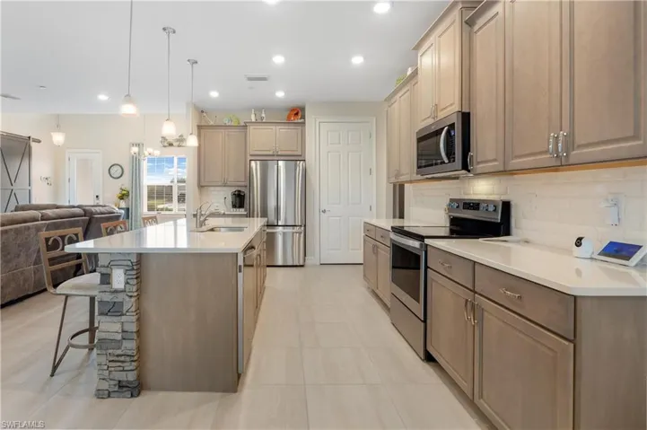 Kitchen featuring light tile patterned floors, appliances with stainless steel finishes, sink, decorative backsplash, and a kitchen island with sink