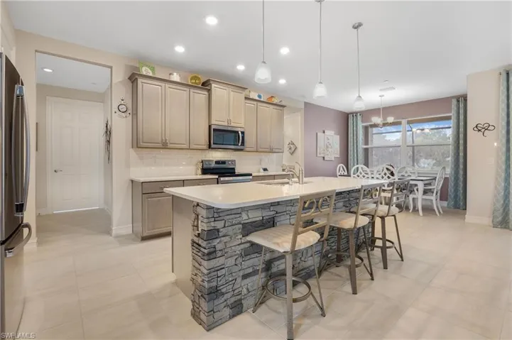 Kitchen with decorative light fixtures, stainless steel appliances, an island with sink, sink, and decorative backsplash