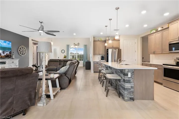 Kitchen with a kitchen island with sink, backsplash, stainless steel appliances, sink, and ceiling fan