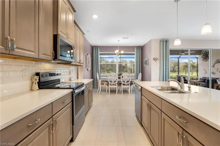 Kitchen with pendant lighting, stainless steel appliances, sink, decorative backsplash, and light tile patterned flooring