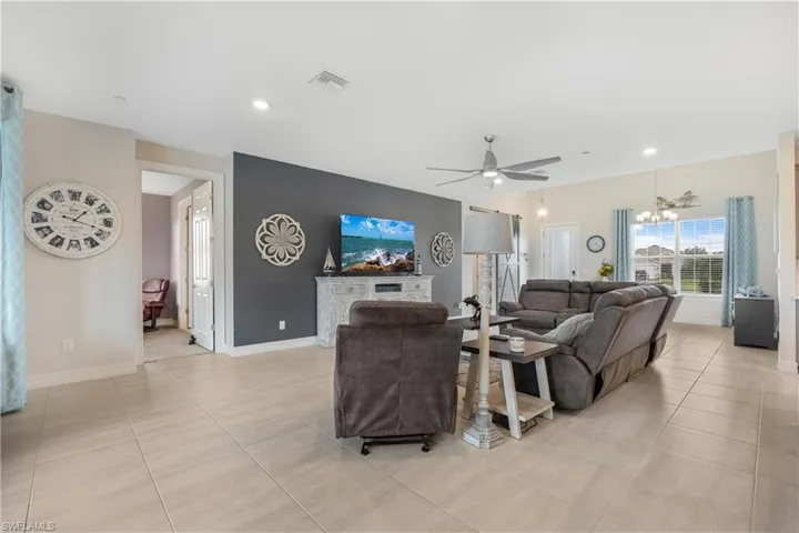 Living room with ceiling fan with notable chandelier and light tile patterned flooring
