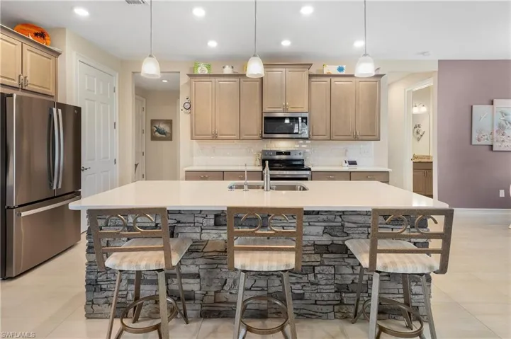 Kitchen featuring hanging light fixtures, sink, appliances with stainless steel finishes, and a kitchen island with sink