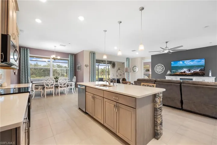 Kitchen featuring ceiling fan with notable chandelier, sink, hanging light fixtures, appliances with stainless steel finishes, and a center island with sink