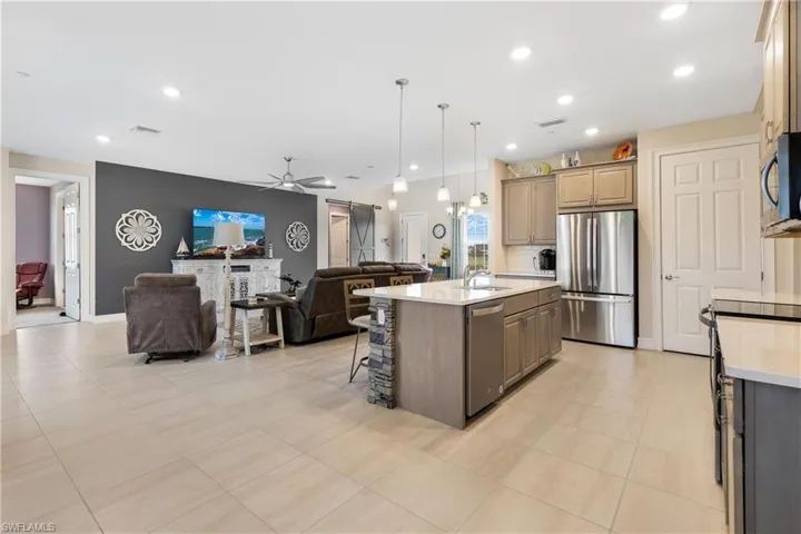 Kitchen featuring a fireplace, appliances with stainless steel finishes, ceiling fan, pendant lighting, and a center island with sink