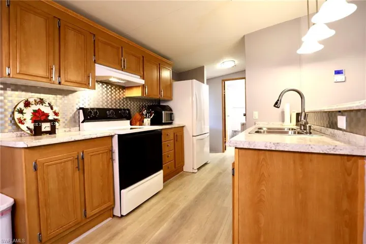 Kitchen with white appliances, tasteful backsplash, sink, light hardwood / wood-style floors, and decorative light fixtures