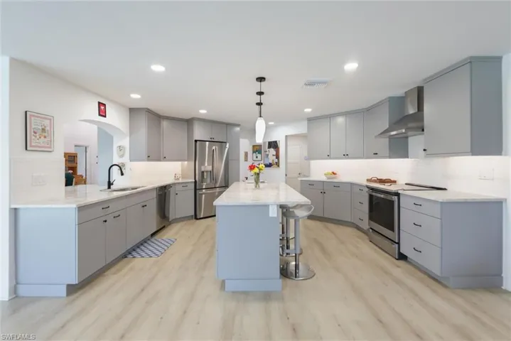 Kitchen featuring gray cabinetry, a kitchen breakfast bar, appliances with stainless steel finishes, wall chimney exhaust hood, and hanging light fixtures