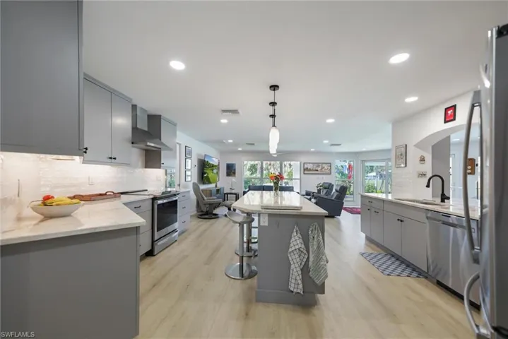 Kitchen with gray cabinetry, backsplash, decorative light fixtures, stainless steel appliances, and open floor plan