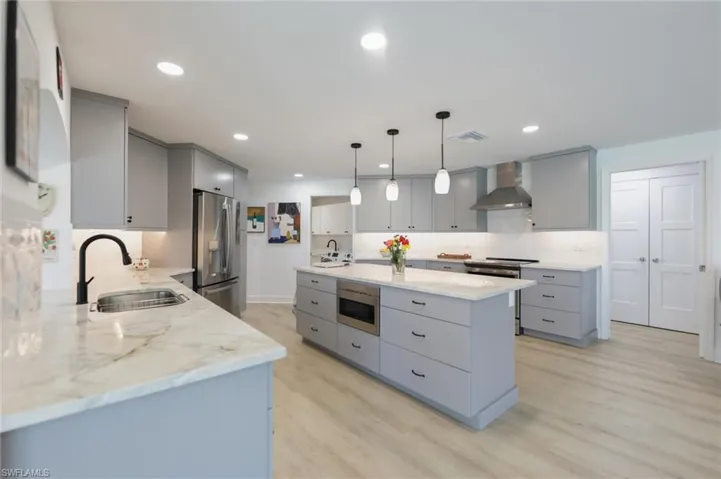 Kitchen featuring gray cabinetry, pendant lighting, wall chimney exhaust hood, stainless steel appliances, and recessed lighting