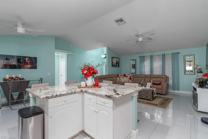 Kitchen with light stone counters, vaulted ceiling, light tile patterned floors, a center island, and white cabinetry