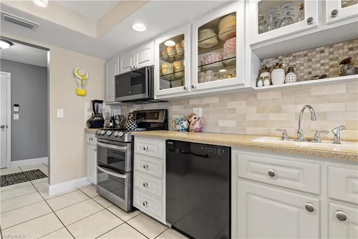 Kitchen featuring white cabinetry, sink, backsplash, light tile patterned floors, and appliances with stainless steel finishes