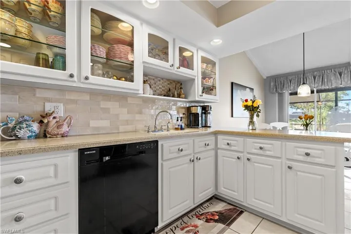 Kitchen featuring sink, vaulted ceiling, light tile patterned floors, black dishwasher, and white cabinetry