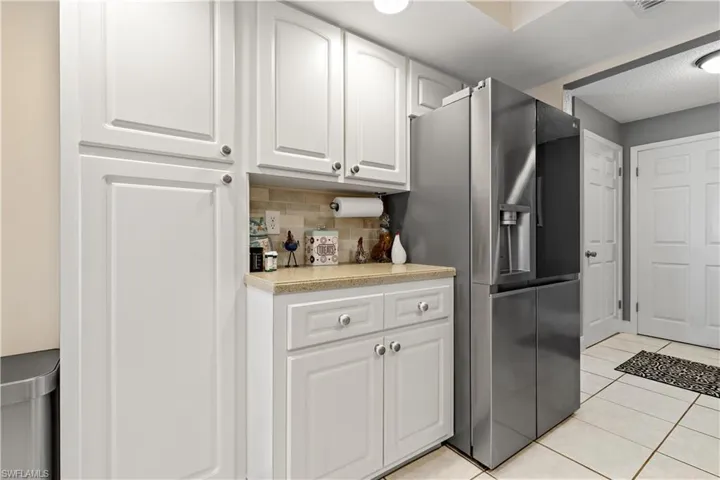 Kitchen with white cabinetry, decorative backsplash, stainless steel fridge, and light tile patterned floors
